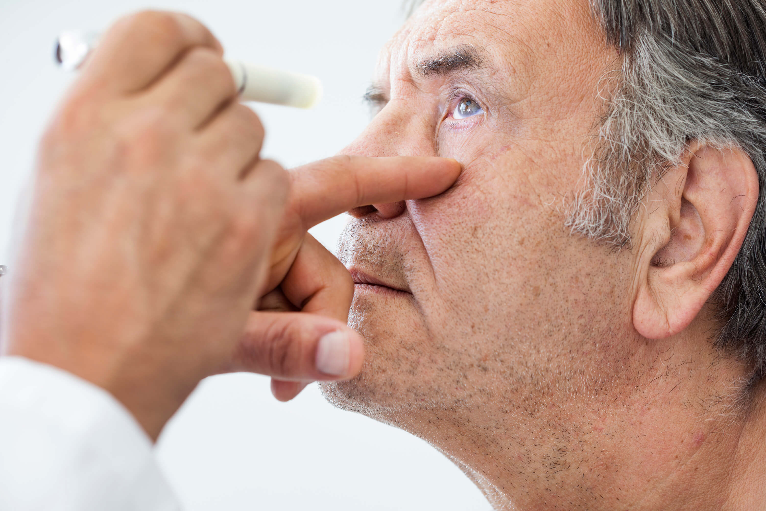 Doctor flashing a light during an eye exam on an older man 