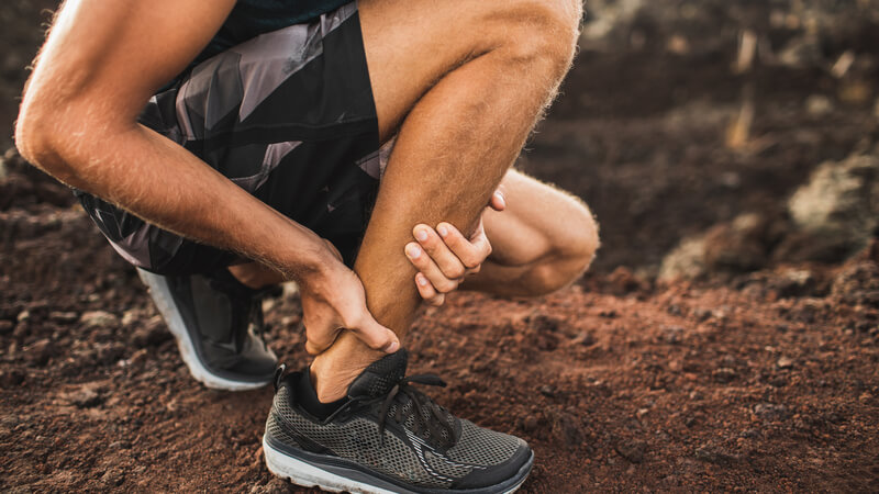 Man crouching down and holding his Achilles heel with his hands